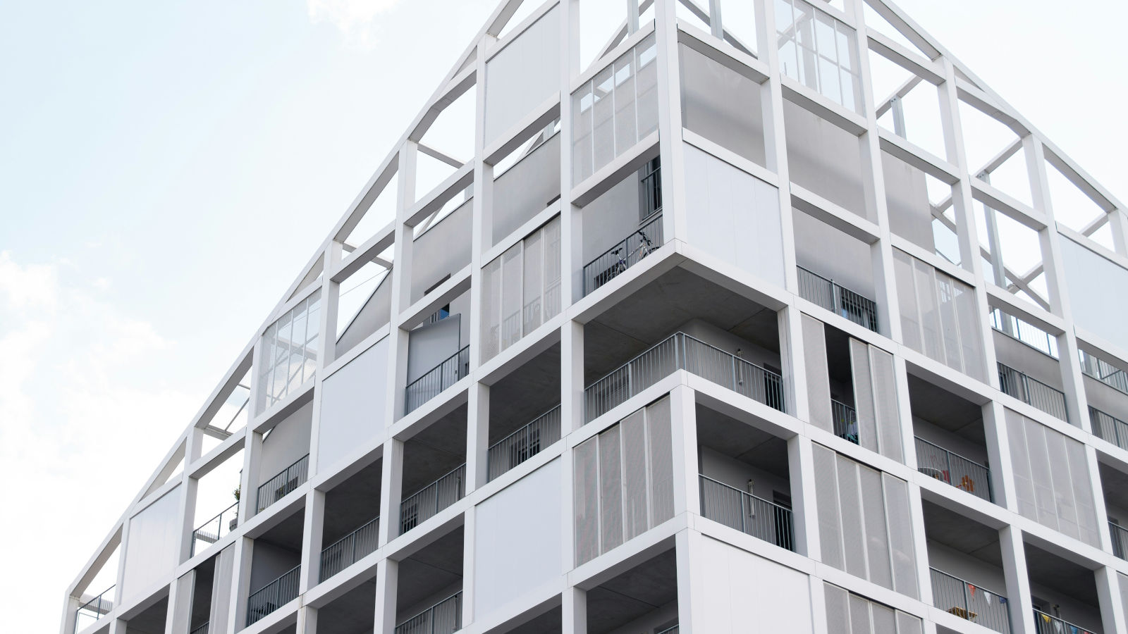 Modern residential building with a white geometric grid facade and open balconies against a bright sky.