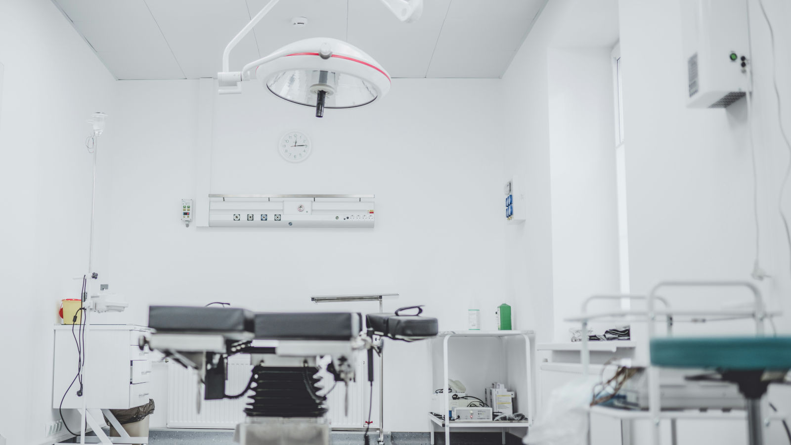 A clean, modern operating room with a surgical table, overhead surgical light, and various medical equipment against white walls.