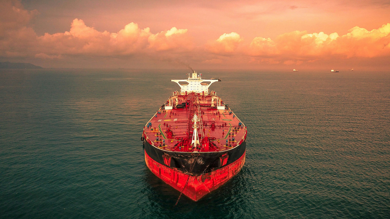 Large oil tanker on the open sea at sunset from an aerial perspective with red and black hull