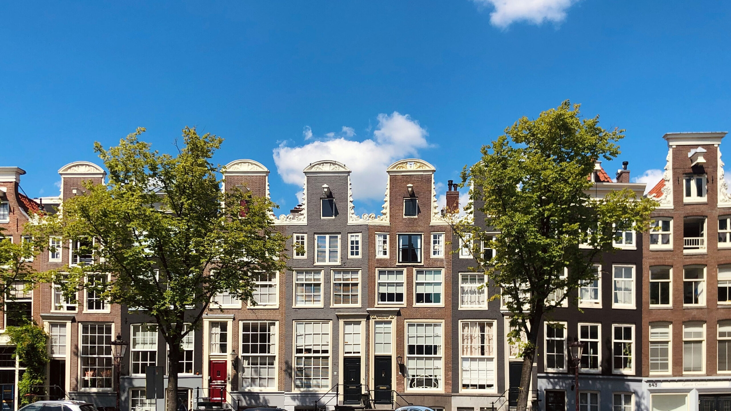 Row of historic Amsterdam canal houses with neck gables and white sash windows beneath a blue sky